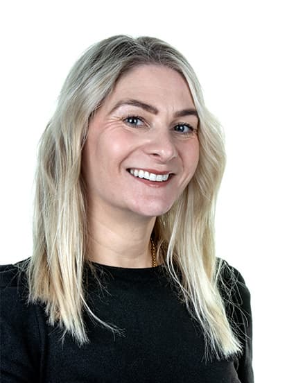 A woman with long blond hair, wearing a black top, smiles at the camera