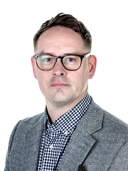 Man wearing glasses, a grey blazer, and a checkered shirt