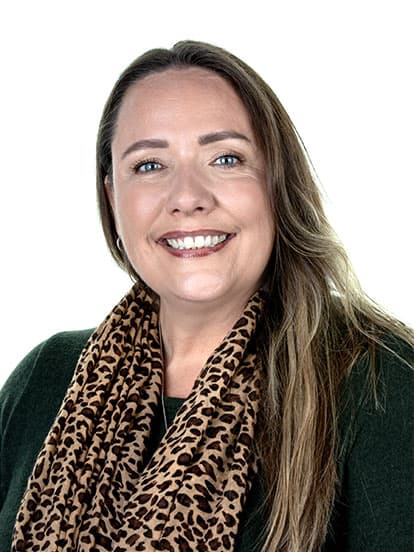 A smiling woman with long brown hair wearing a leopard print scarf and green top