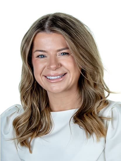Smiling woman with wavy brown hair, wearing a white blouse
