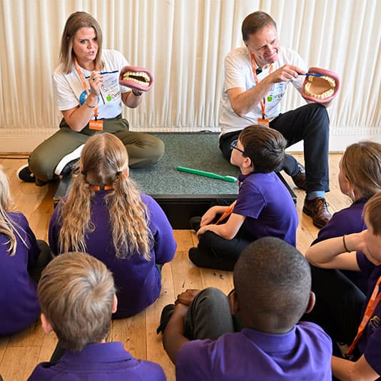 A group of children sitting on the floor, watching a demonstration on teeth brushing