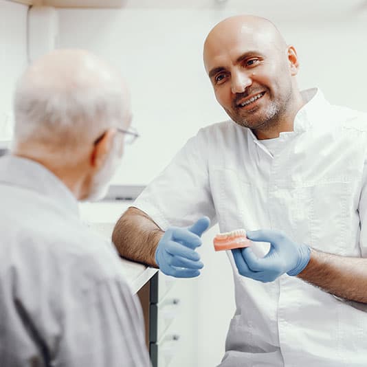 Man talking to dentist holding dentures